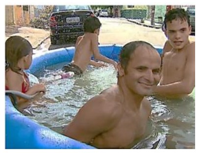 Fotografia que acompanha a notícia: pessoas dentro de uma piscina de plástico azul na rua.