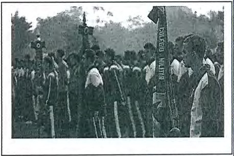 Fotografia de alunos uniformizados em formatura ao ar livre, com um estandarte com a inscrição "Colégio Militar".