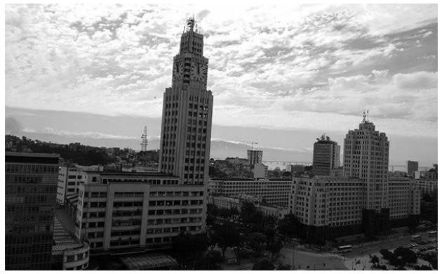 Fotografia em preto e branco do prédio da Central do Brasil, com sua torre do relógio, e edifícios ao redor no Rio de Janeiro.