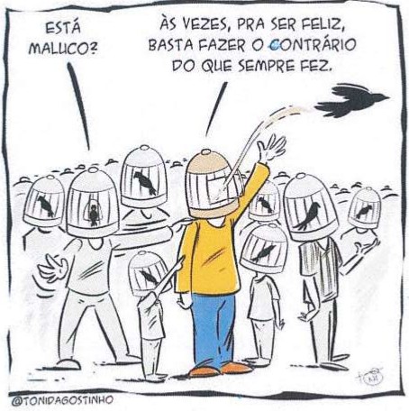 Cartum de Toni D'Agostinho: uma multidão de pessoas, todas com gaiolas na cabeça contendo pássaros pretos presos. No centro, um homem de camisa amarela e calça azul abriu a própria gaiola e solta o pássaro, que voa para longe. Ele diz: “Às vezes, pra ser feliz, basta fazer o contrário do que sempre fez.” Uma pessoa ao lado pergunta: “Está maluco?”. Assinatura: @TONIDAGOSTINHO.