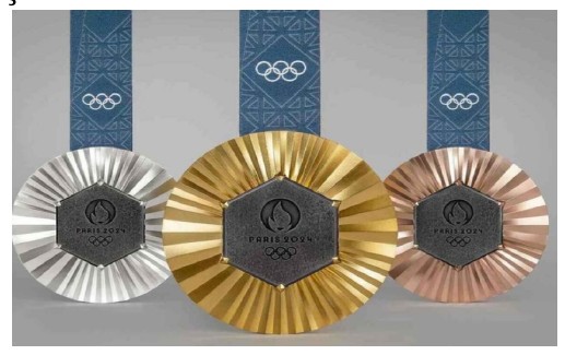 Fotografia das três medalhas dos Jogos de Paris 2024 (prata, ouro e bronze), com o centro hexagonal escuro e fitas azuis com os anéis olímpicos.