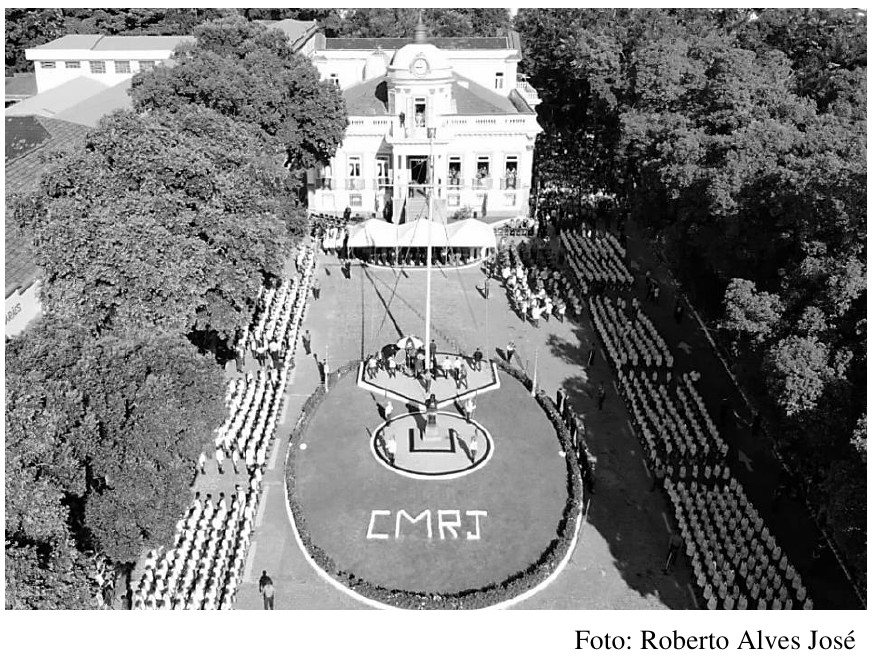 Foto aérea em preto e branco da Praça Thomaz Coelho, com o prédio do CMRJ ao fundo, alunos em formação dos dois lados e, no centro, um palco pentagonal e um palco circular com as letras CMRJ. Crédito: Foto: Roberto Alves José.