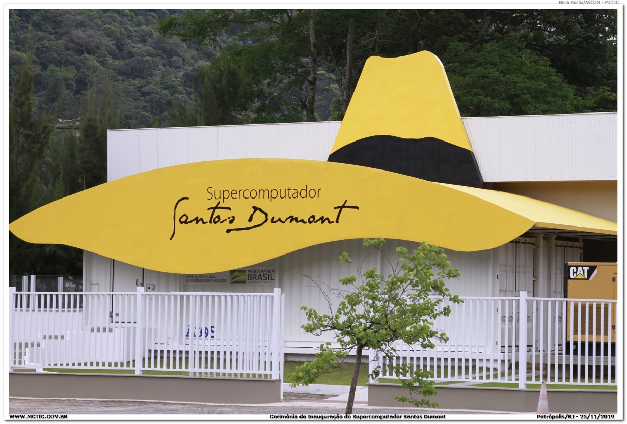 Fotografia do prédio do Supercomputador Santos Dumont, com uma grande escultura de chapéu amarelo com faixa preta sobre a fachada branca, onde se lê “Supercomputador Santos Dumont”.