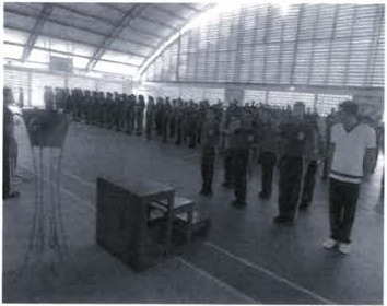 Fotografia de alunos uniformizados em formação dentro de um ginásio coberto.