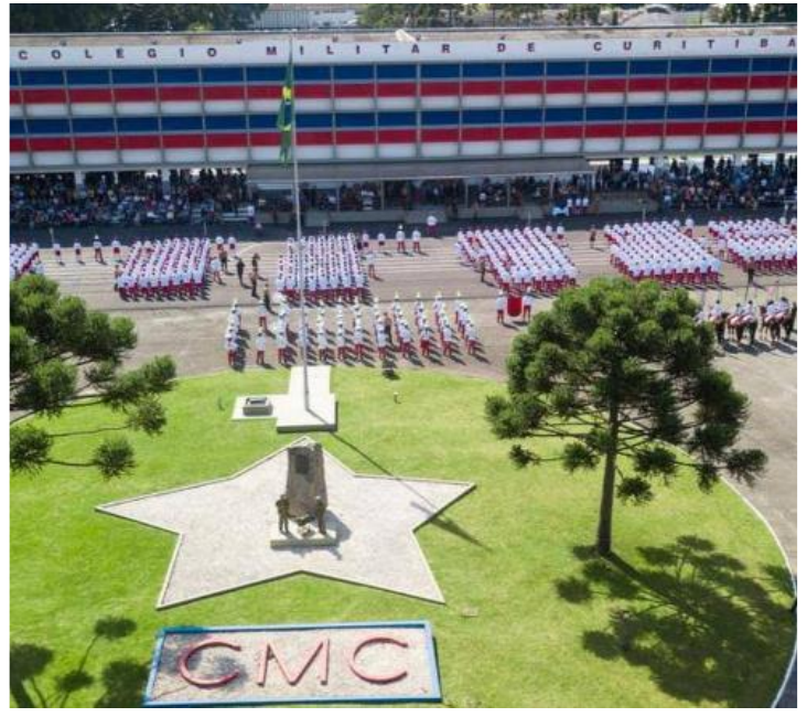 Fotografia aérea do pátio de formatura do Colégio Militar de Curitiba com alunos em formação, mastro com a bandeira do Brasil, canteiro em forma de estrela e letreiro CMC.