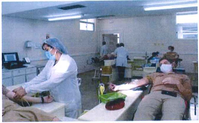 Fotografia de uma sala de coleta de sangue: profissional de touca e máscara atende doador; ao fundo, outros doadores em poltronas reclináveis.