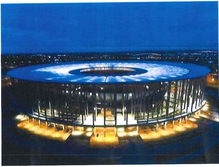 Fotografia noturna aérea do Estádio Mané Garrincha iluminado, em Brasília.