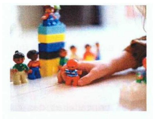 Fotografia de uma mão de criança brincando com bonecos e blocos de montar coloridos sobre uma mesa.