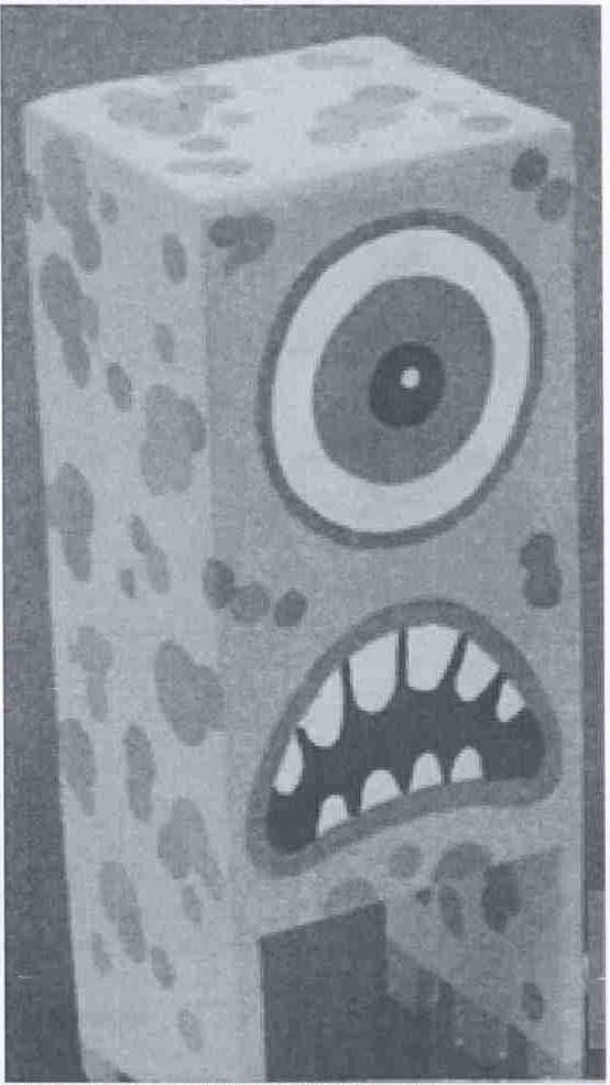 Fotografia de um monstro de papelão em forma de bloco retangular, pintado com manchas, um olho grande e boca com dentes.