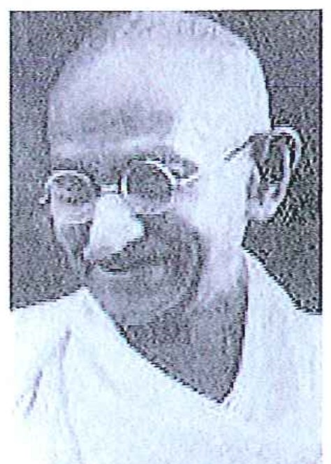 Fotografia em preto e branco de Mahatma Gandhi, idoso, calvo, de óculos redondos, sorrindo.