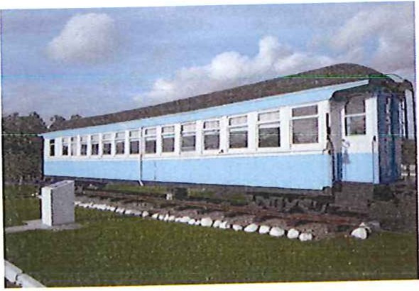 Fotografia de um vagão de trem azul-claro exposto sobre trilhos em área gramada.