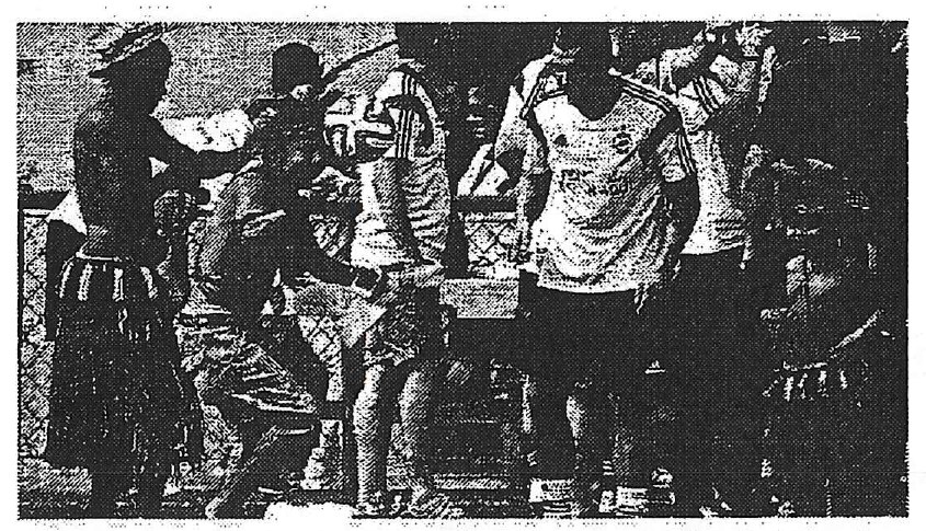 Fotografia em preto e branco: jogadores com uniforme da seleção alemã de futebol ao lado de pessoas com trajes indígenas, em ambiente externo.