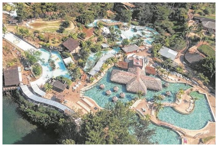 Fotografia aérea do parque aquático Hot Park, com várias piscinas de água azul-esverdeada, quiosques com cobertura de palha, construções e vegetação ao redor.