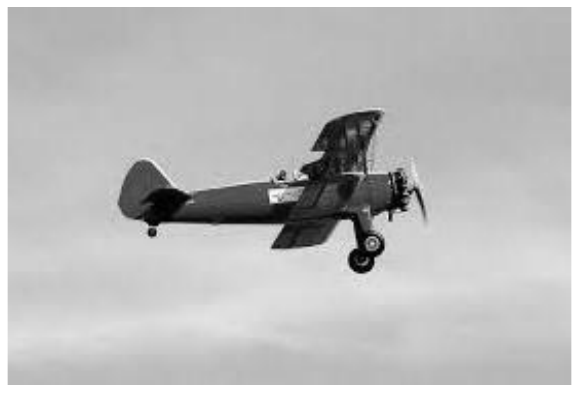 Fotografia de um avião biplano com hélice frontal voando.
