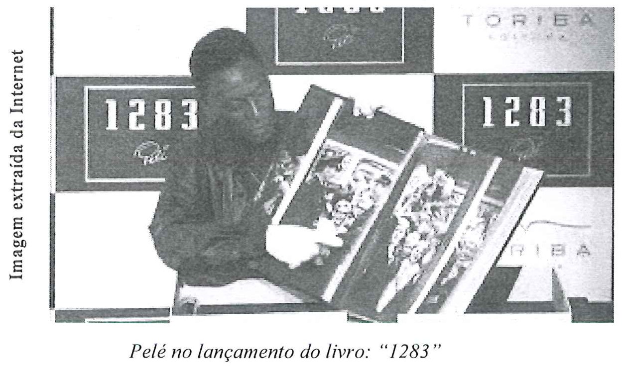 Fotografia de Pelé segurando um exemplar aberto do livro "1283" diante de painéis com o título do livro, com a legenda impressa "Pelé no lançamento do livro: “1283”".