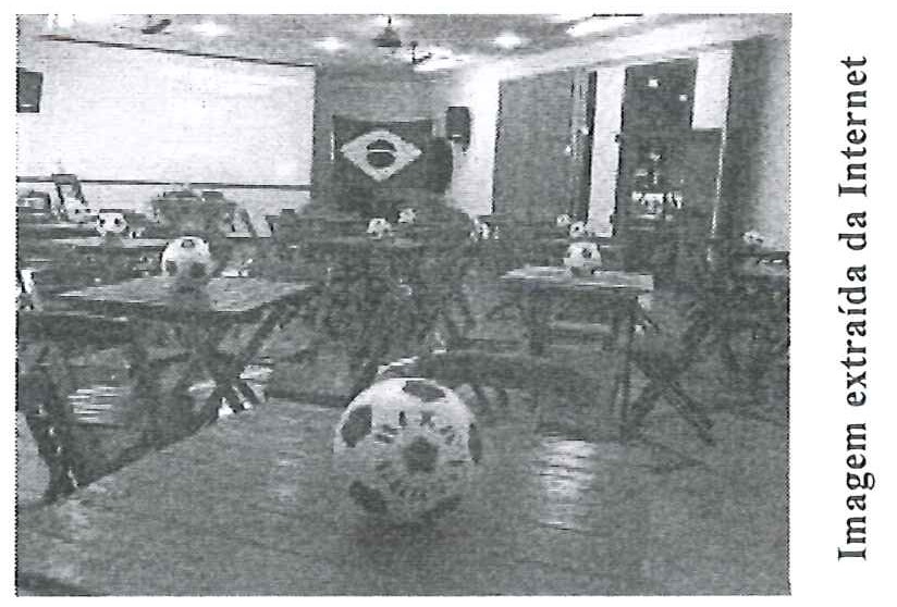 Fotografia do interior de um bar decorado com bolas de futebol sobre as mesas e uma bandeira do Brasil ao fundo.
