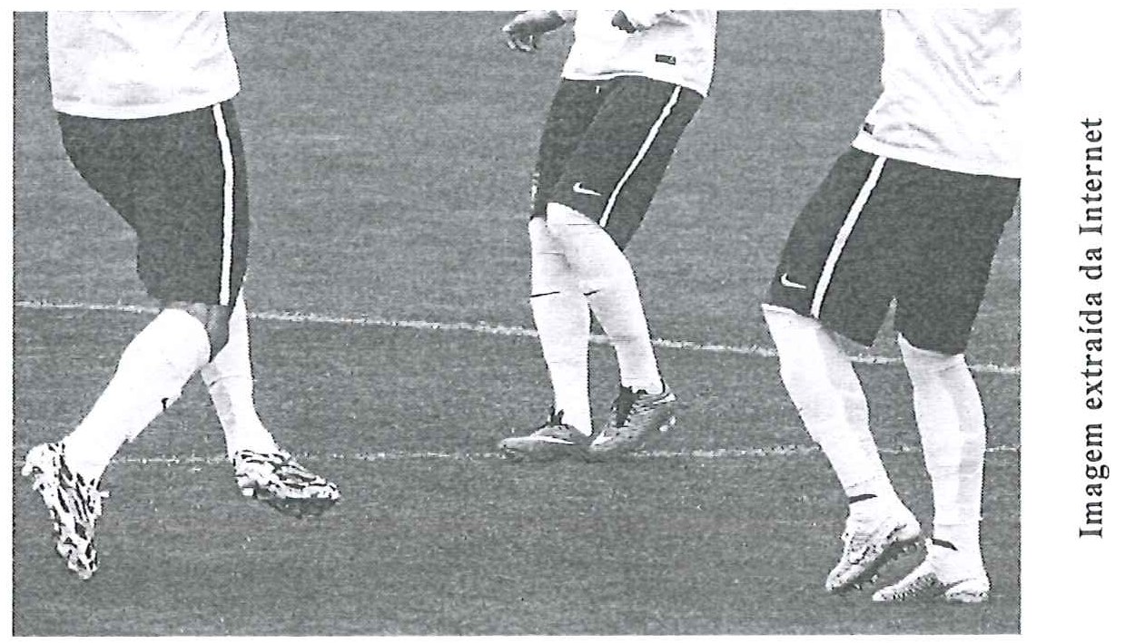 Fotografia das pernas de jogadores em treino no gramado, usando chuteiras.