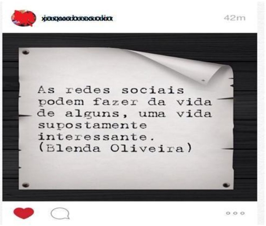 Postagem de rede social (Instagram), com nome de usuário ilegível/rasurado e indicação “42m”. Sobre um papel pregado em fundo de madeira escura, o texto: “As redes sociais podem fazer da vida de alguns, uma vida supostamente interessante. (Blenda Oliveira)”. Abaixo, ícones de coração, comentário e reticências.
