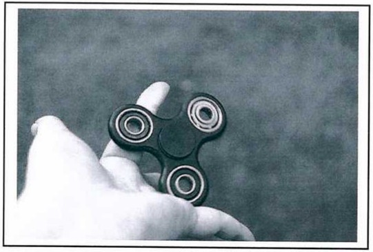 Fotografia de uma mão segurando um fidget spinner de três pontas com rolamentos.