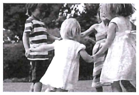 Fotografia em preto e branco de crianças de mãos dadas brincando de roda ao ar livre.