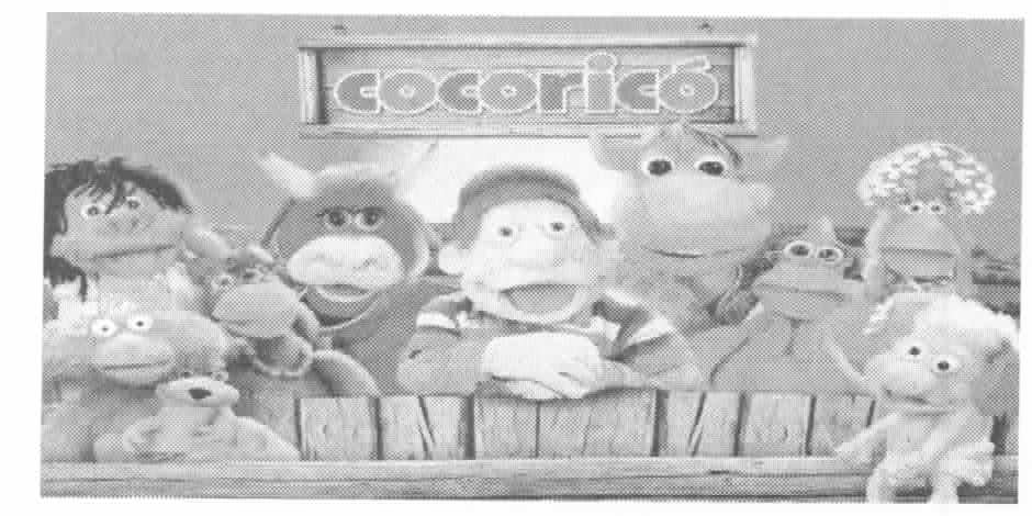 Fotografia dos bonecos do programa Cocoricó reunidos atrás de uma cerca de madeira, sob a placa com o nome “Cocoricó”.