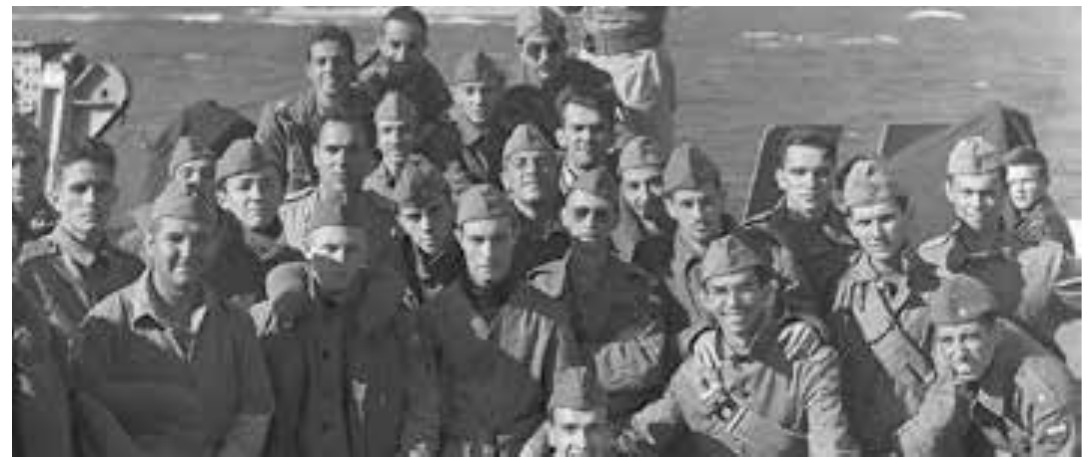 Fotografia em preto e branco de um grupo de soldados brasileiros da FEB, de quepe e uniforme, reunidos no convés de um navio.