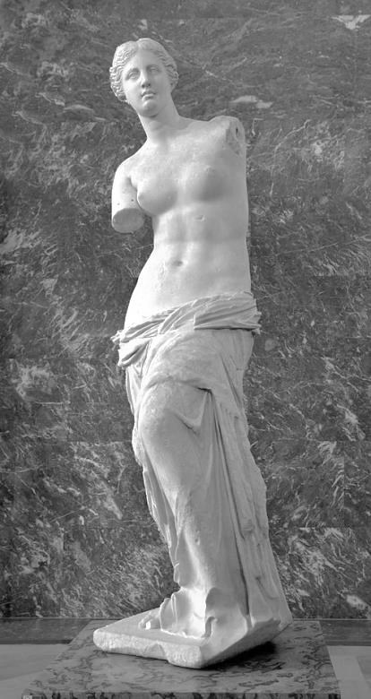 Fotografia em tons de cinza da escultura Vênus de Milo: estátua de mármore de figura feminina de pé, sem os braços, com o torso nu e um manto drapeado envolvendo os quadris e as pernas, sobre um pedestal, diante de uma parede de mármore escuro.