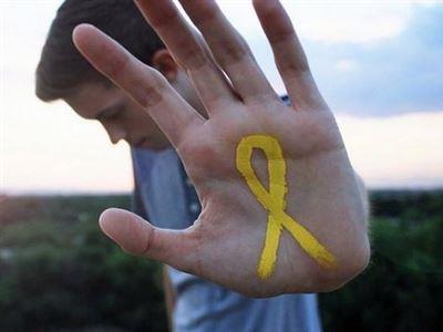 Fotografia de um jovem estendendo a palma da mão aberta em direção à câmera; na palma está desenhado um laço amarelo (símbolo do Setembro Amarelo).