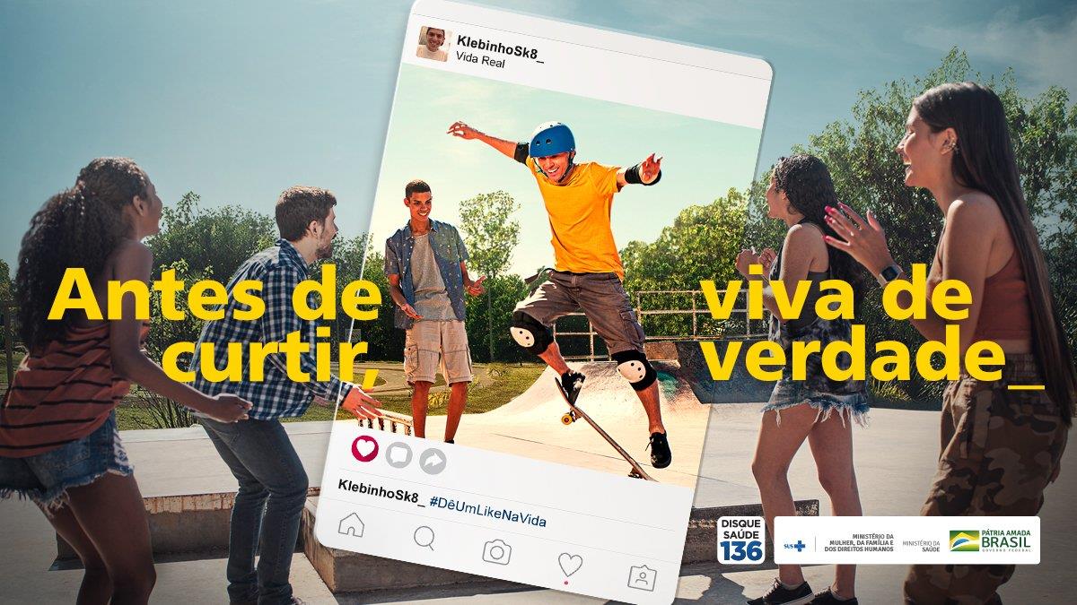Peça publicitária: jovens se divertindo ao ar livre, um deles saltando de skate, enquadrados por uma moldura de postagem de rede social (perfil “Kleb1nho_”, “Vida Real”, hashtag “#DêUmLikeNaVida”). Texto em amarelo: “Antes de curtir, viva de verdade_”. No canto inferior direito: “Disque Saúde 136” e logotipos do Governo Federal (Brasil).